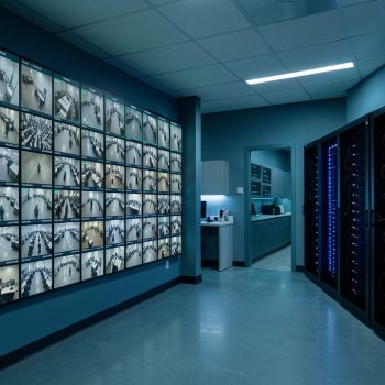 Centre de supervision sécurisé avec un mur d’écrans de vidéosurveillance, des cadres discrets d’analyse automatisée et des serveurs GPU visibles.