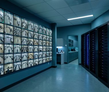 Centre de supervision sécurisé avec un mur d’écrans de vidéosurveillance, des cadres discrets d’analyse automatisée et des serveurs GPU visibles.
