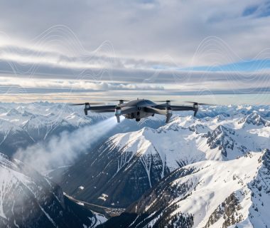 Drone VTOL d’ensemencement survolant des montagnes enneigées sous des nuages froids, avec une visualisation discrète de données météorologiques abstraites.